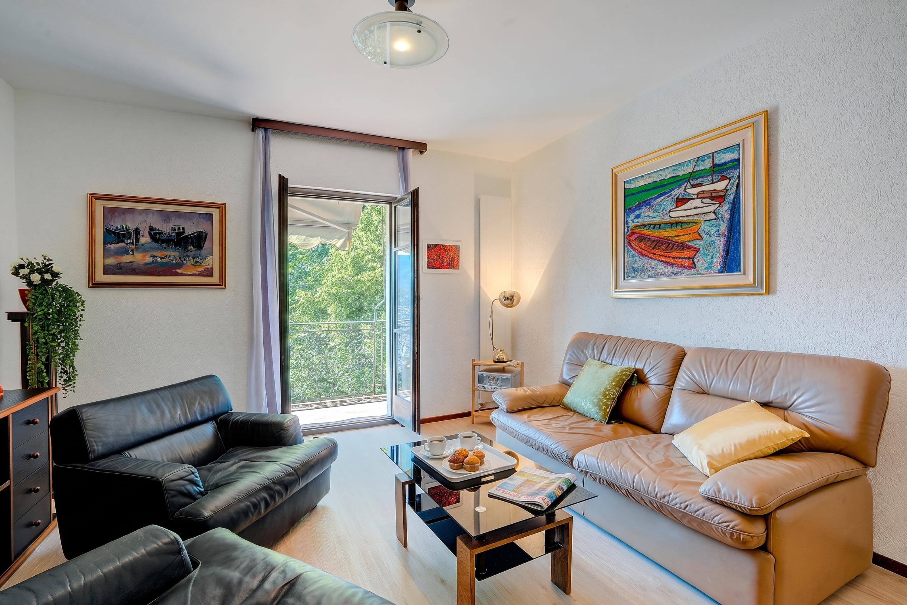 Ein Wohnzimmer mit einem schwarzen Ledersofa, einem beigen Sofa mit Kissen, einem Couchtisch mit Zeitschrift und Muffinblech sowie einem Bild an der Wand.