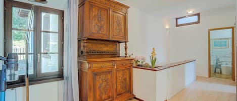 A room with a wooden cabinet, a window with a view, a ceiling light, and a mirror on the wall.