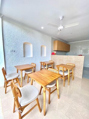 A dining area with wooden tables and chairs, a ceiling fan, and a kitchen in the background. - Desri Ubud (Ubud)