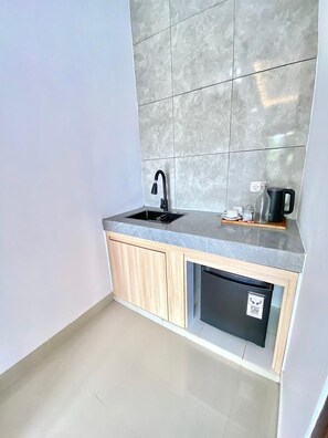 A compact kitchen with a built-in dishwasher, a black faucet, and a coffee maker on the countertop. - Desri Ubud (Ubud)