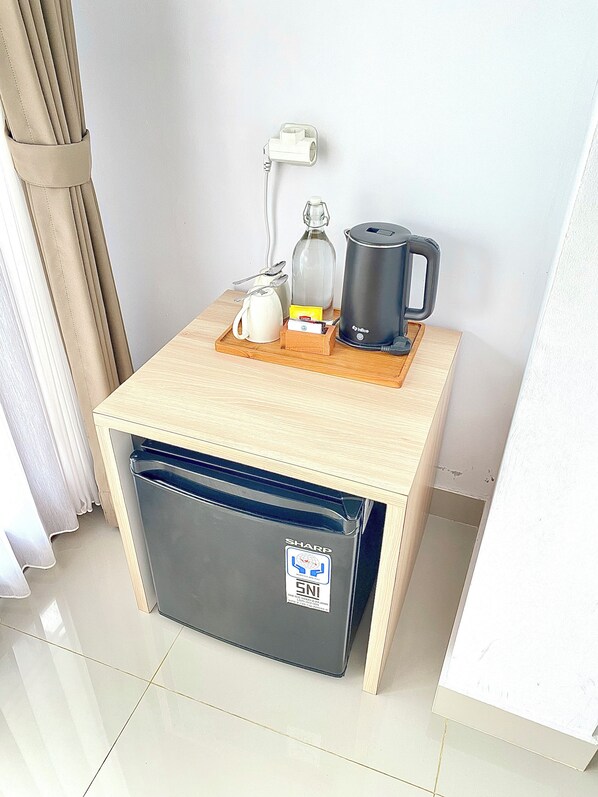 A compact kitchenette with a coffee maker, kettle, and a bottle on a wooden tray.