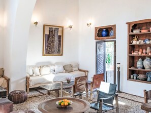 Een gezellige woonkamer met een bank, stoelen, een bijzettafeltje met fruit, een decoratief wandobject en een plank met potten.