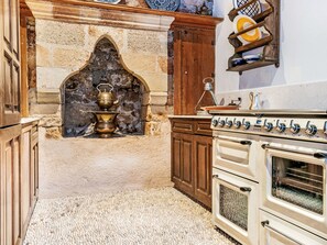 A kitchen with a stone archway, a stove, wooden cabinets, and a shelf with dishes. - Vasilikos Mansion by Interhome (Pefki)