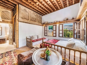 A traditional room with a wooden ceiling, a bed with a red patterned bedspread, a sofa, and a view of a mountainous landscape through a window. - Vasilikos Mansion by Interhome (Pefki)