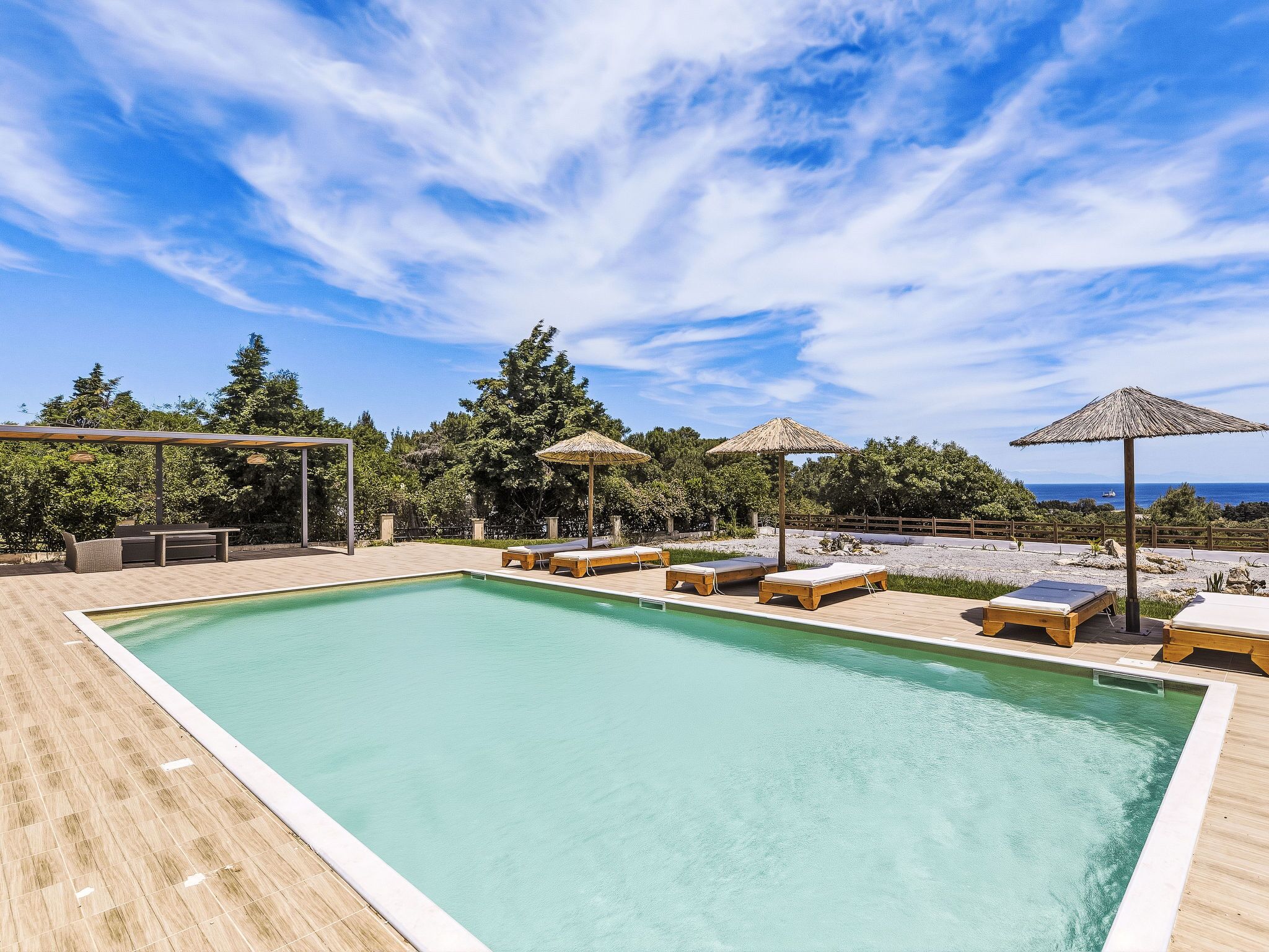 Une piscine rectangulaire entourée d’arbres et dotée d’une terrasse en bois, avec des chaises longues et des parasols.