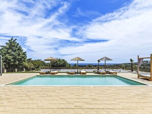 Ein Pool mit Liegestühlen und Sonnenschirmen, umgeben von einer Holzterrasse und Bäumen.