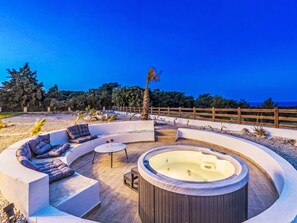 Ein runder Außenbereich mit Whirlpool, umgeben von einer Holzterrasse und einer niedrigen Mauer.