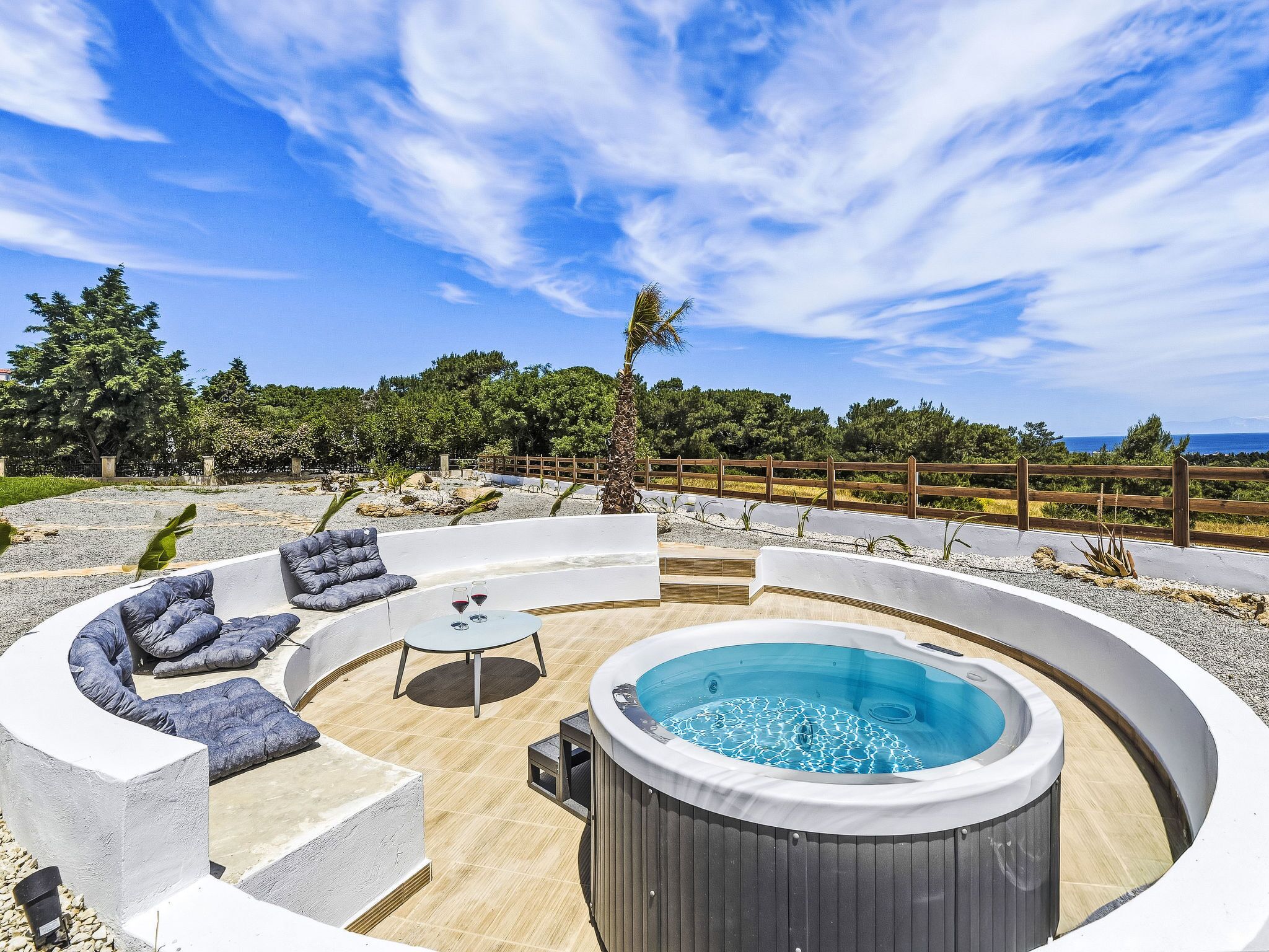 Un jacuzzi rodeado por una zona de asientos curva con cojines, una valla de madera y vista al mar.