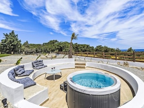 Ein Whirlpool, umgeben von einer bogenförmigen Sitzgruppe mit Kissen, einem Holzzaun und Blick auf das Meer.