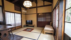 A traditional Japanese room with tatami flooring, a television, a wooden table, and a sliding door. - Magoichi: A Traditional Japanese House Condominium Available for Entire-Property Rentals (加賀市橋立町)