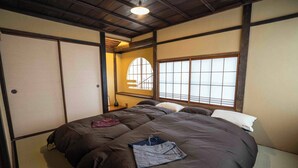 A traditional Japanese-style room with tatami flooring, a shoji screen door, a futon bed, and a window with a grid pattern. - Magoichi: A Traditional Japanese House Condominium Available for Entire-Property Rentals (加賀市橋立町)