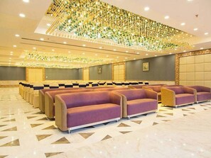 Eine geräumige Lobby mit Reihen violetter Sitzgelegenheiten, einer dekorativen Decke und einem gemusterten Boden.