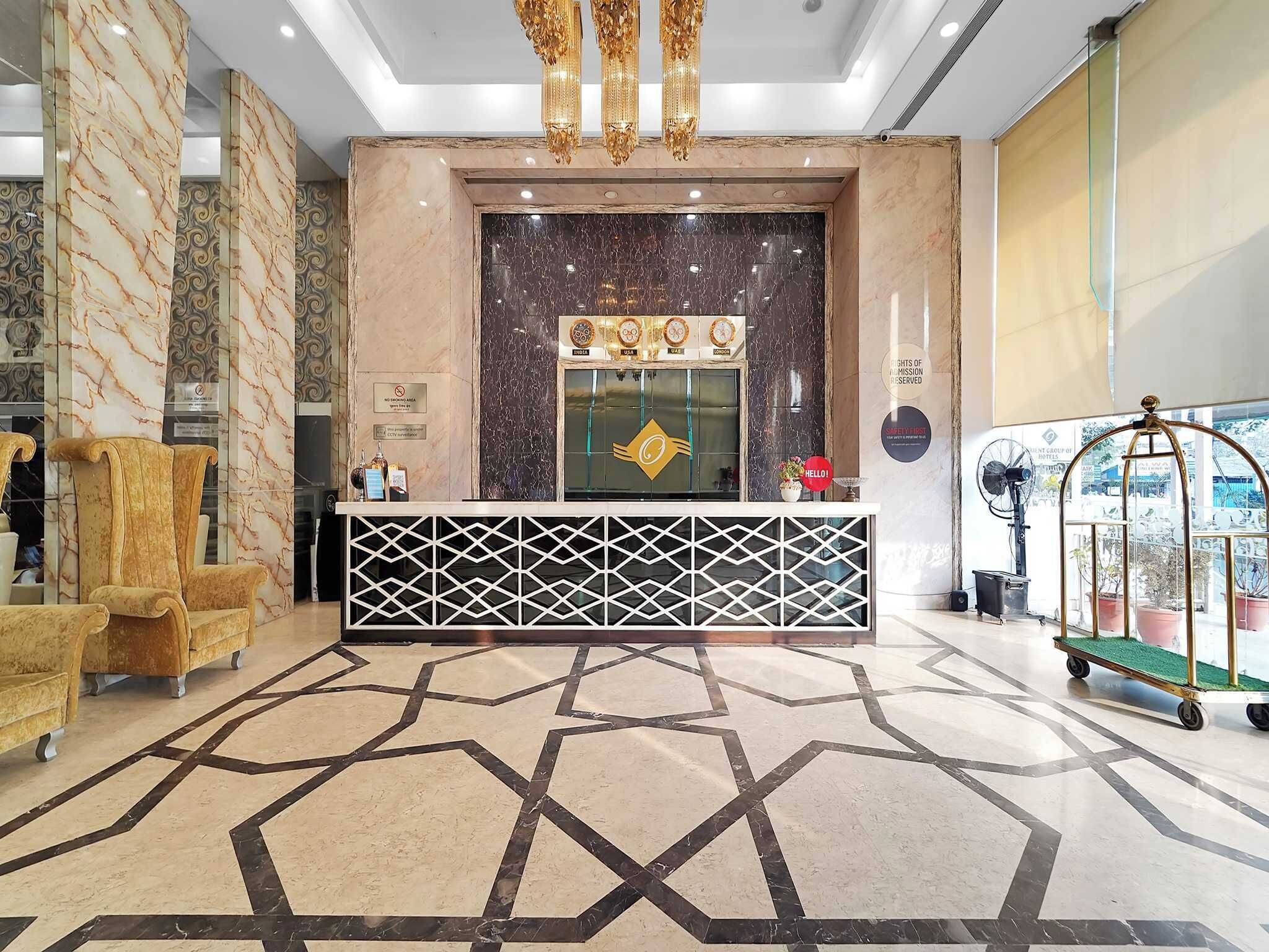 Un mostrador de recepción con piso de diseño geométrico, una araña y una sala de espera con pared de mármol.