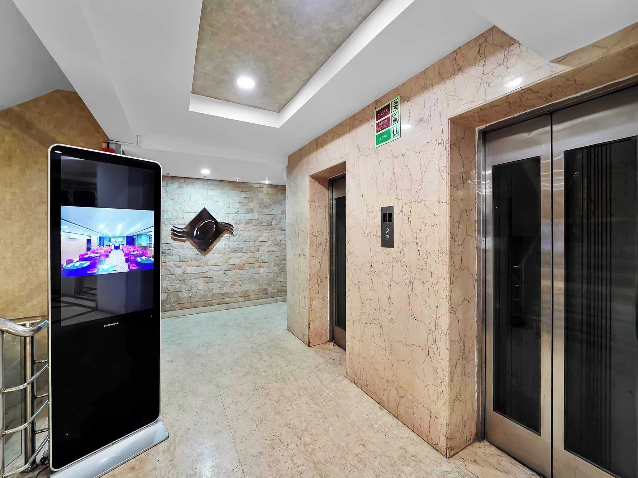Un pasillo con una pantalla digital, ascensores y una pared de piedra.