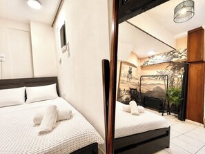 Ein Hotelzimmer mit zwei Betten, einem großen Spiegel, einem an der Wand befestigten Fernseher und einem Wandbild mit einer tropischen Landschaft.