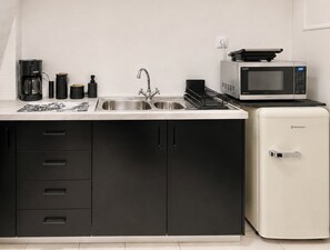 Eine kleine Küche mit Spüle, Kaffeemaschine, Mikrowelle und Kühlschrank.