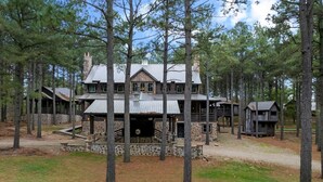 A large log cabin with a stone foundation, multiple levels, and a chimney. - Themed Cabin+Treehouse | 5 King Suites | Sleeps 23 (Broken Bow)