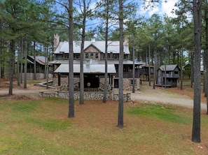 A large log cabin with a stone foundation, multiple levels, and a chimney. - Themed Cabin+Treehouse | 5 King Suites | Sleeps 23 (Broken Bow)