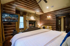 A bedroom with a stone fireplace, wooden walls, a bed, and a painting of a castle. - Wizard Cabin+Treehouse | Game Zone | Sleeps 23 (Broken Bow)