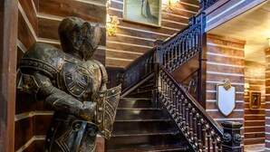 A wooden staircase with a metal railing, a statue of a knight, and a shield on the wall. - Themed Cabin+Treehouse | 5 King Suites | Sleeps 23 (Broken Bow)