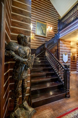 A wooden staircase with a metal railing, a statue of a knight, and a shield on the wall. - Themed Cabin+Treehouse | 5 King Suites | Sleeps 23 (Broken Bow)