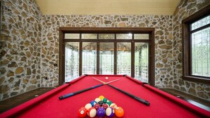 A pool table with balls and cues, set against stone walls with large windows. - Themed Cabin+Treehouse | 5 King Suites | Sleeps 23 (Broken Bow)