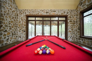 A pool table with balls and cues, set against stone walls with large windows. - Themed Cabin+Treehouse | 5 King Suites | Sleeps 23 (Broken Bow)