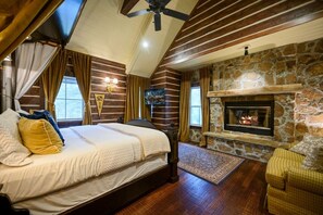 Un dormitorio con una cama grande, una chimenea de piedra y un ventilador de techo.