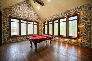 A pool room with a pool table, stone walls, and large windows. - Wizard Cabin+Treehouse | Game Zone | Sleeps 23 (Broken Bow)