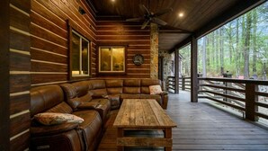 A log cabin interior with a wooden deck, a leather sofa, and a wooden table. - Themed Cabin+Treehouse | 5 King Suites | Sleeps 23 (Broken Bow)