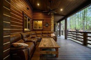A log cabin interior with a wooden deck, a leather sofa, and a wooden table. - Themed Cabin+Treehouse | 5 King Suites | Sleeps 23 (Broken Bow)