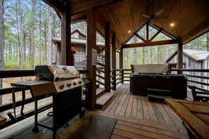 Terraza al aire libre con una parrilla y un jacuzzi, rodeada de estructuras de madera y árboles.