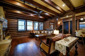 Interno di una baita in legno con pavimento in legno, un divano, un tavolo da pranzo con tovaglia in pizzo e un camino.