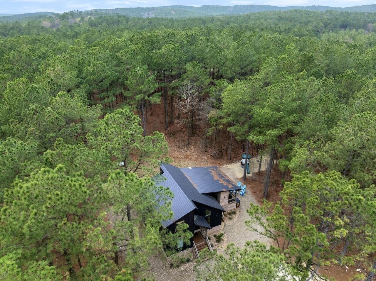 Une cabane entourée d’une forêt dense, avec un chemin de gravier menant à celle-ci.