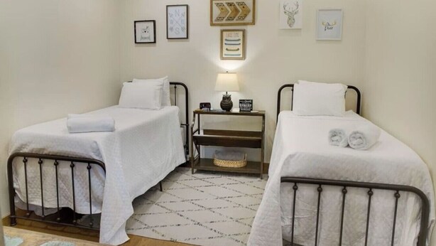 Quarto com duas camas de solteiro, uma mesa de cabeceira com abajur e uma pintura na parede.