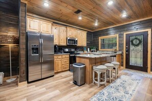 A modern kitchen with wooden cabinets, stainless steel appliances, and a bar area with stools. - 2 King Suites | Hot Tub+Game Room | Sleeps 8 (Broken Bow)