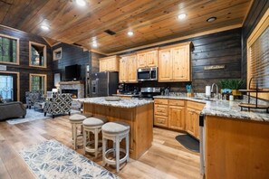 A modern kitchen with wooden cabinets, a large island, and bar stools. - 2 King Suites | Hot Tub+Game Room | Sleeps 8 (Broken Bow)