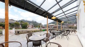 Una terrazza esterna con tavoli e sedie, un tetto in vetro e vista su edifici tradizionali sullo sfondo.
