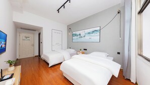Quarto de hotel com piso de madeira, duas camas, televisão de tela plana, um quadro e uma janela com cortinas.