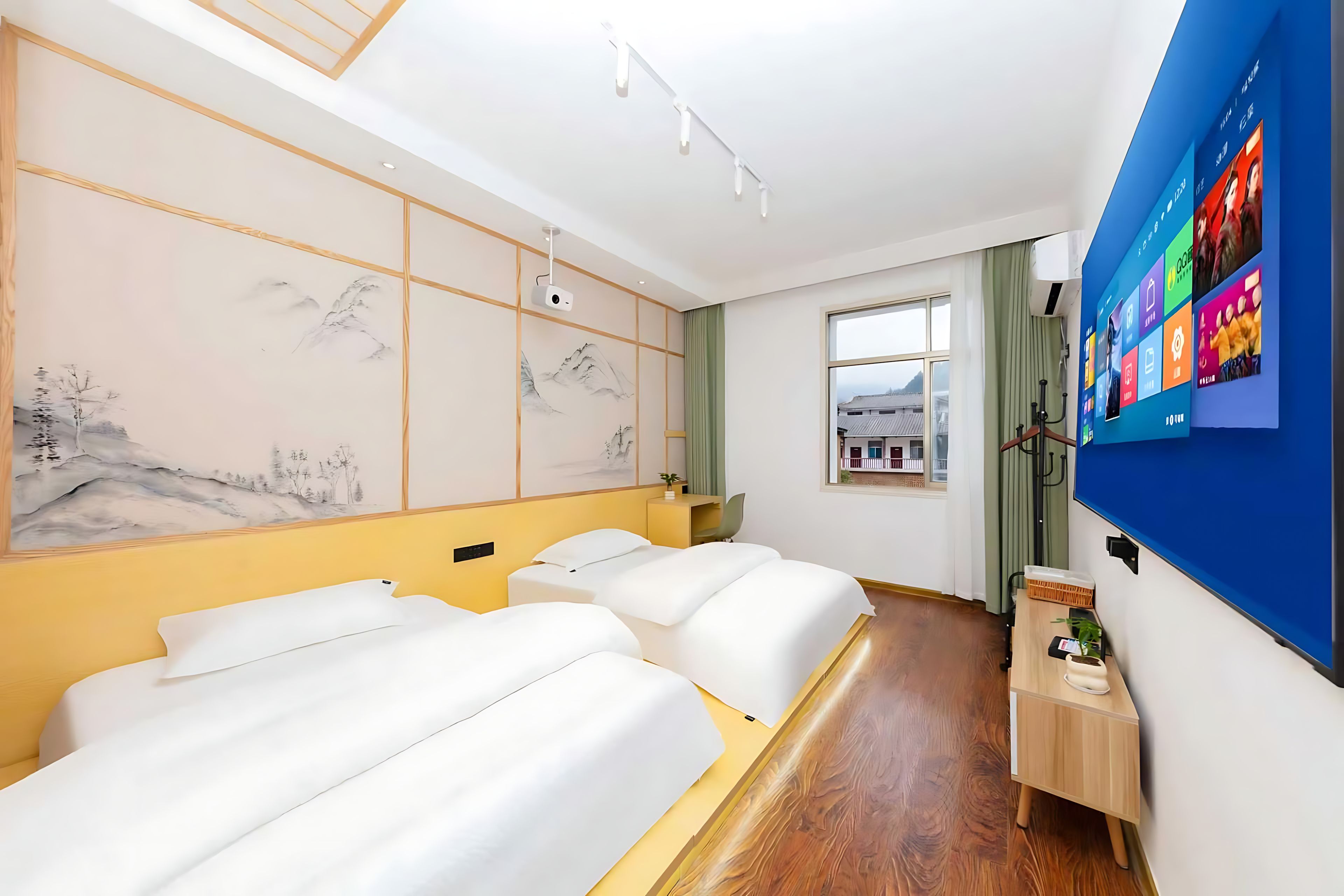 A hotel room with two beds, a large window, a wall-mounted TV, and a projector.