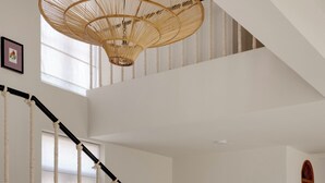 A dining area with a round table, chairs, a hanging light fixture, and a staircase with a rope railing. - Staymaster Cove Villa (Parra)