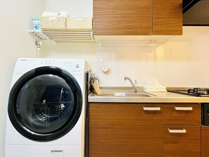 A compact kitchen with a built-in washing machine, a sink, and wooden cabinets. - [Perfect for Sightseeing in Tokyo] 3-minute walk from the station | 1LDK | Sleeps 4 | Families Welcome (港区浜松町)