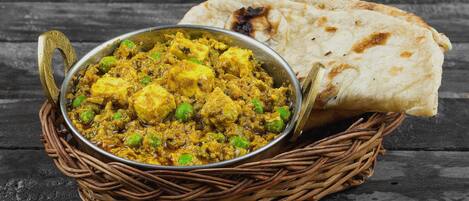 A dish of paneer curry with naan bread on a rustic wooden table.