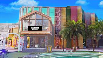 A modern building with a glass facade, a pool area with lounge chairs, and a decorative archway.