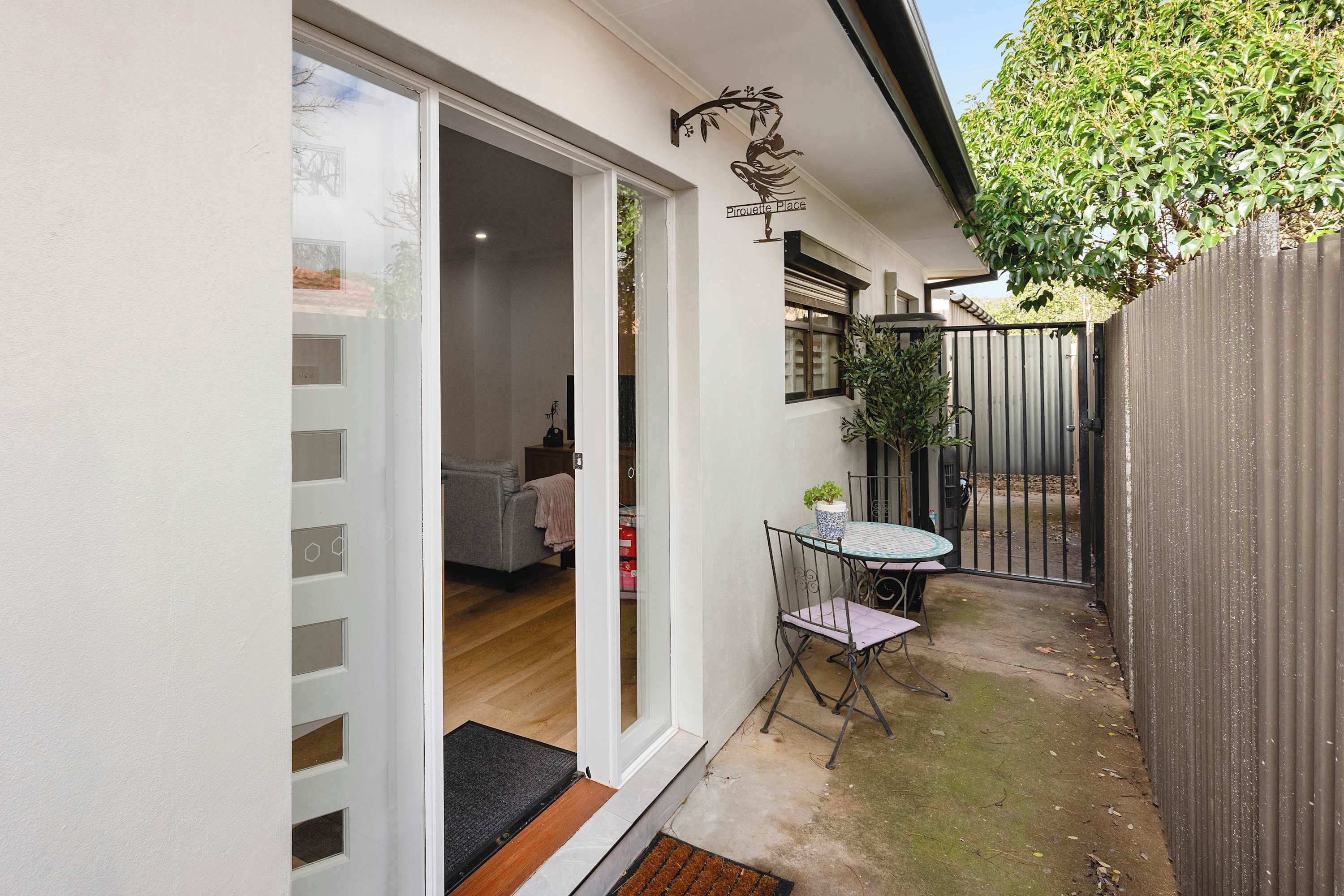 Propiedad residencial con puerta corrediza de vidrio, un pequeño patio con mesa y sillas, y un jardín cercado.