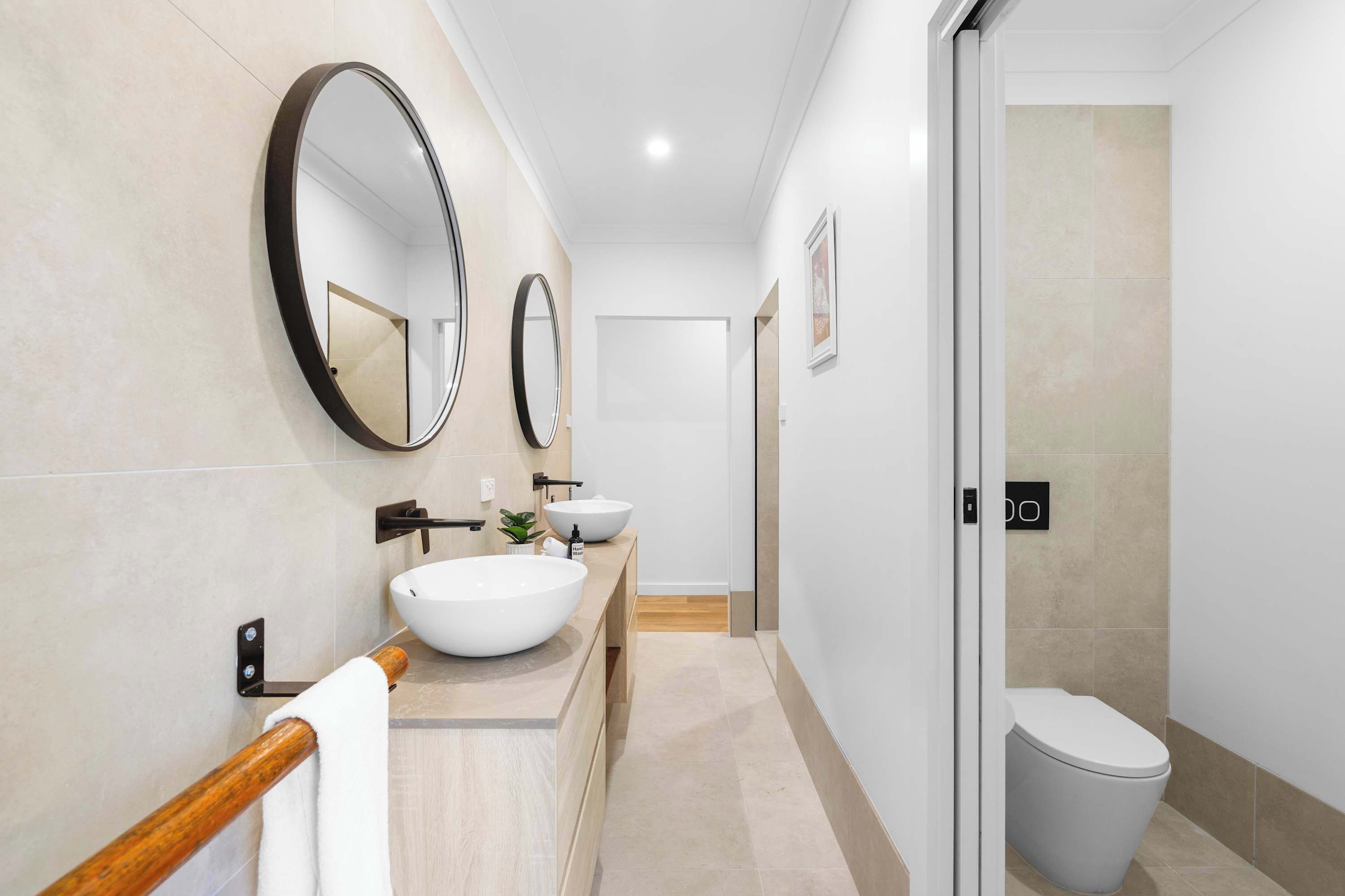 A modern bathroom with a wooden vanity, two round mirrors, a white sink, and a toilet.
