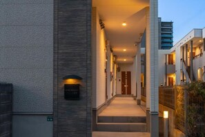 Un pasillo de hotel con una escalera que conduce a la entrada, un cartel que indica la ubicación y una fachada de edificio moderna.
