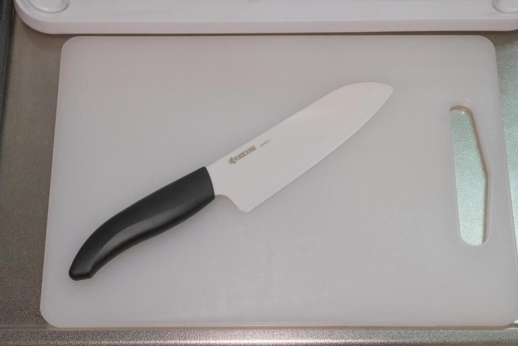 Uma bancada de cozinha com uma tábua de corte branca, uma faca e um objeto retangular pequeno.