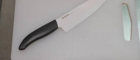 Uma bancada de cozinha com uma tábua de corte branca, uma faca e um objeto retangular pequeno.