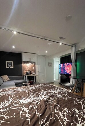 A modern bedroom with a large bed, a television, a desk, and a kitchenette.